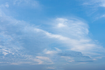 Wispy white cirrus and altocumulus clouds drift across a bright blue sky expanse