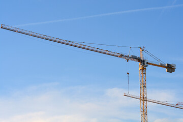 Two yellow construction cranes are positioned against a bright blue sky during an urban development project
