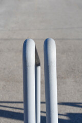 A detailed vertical shot of the rounded tops of a white painted metal handrail with a blurred grey concrete background.