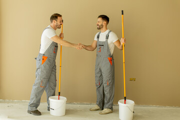 Two workers shake hands in a room after painting tasks are completed