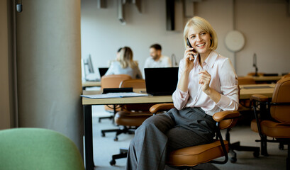 Woman speaking on phone in a workspace while colleagues work at desks