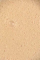 A top down macro view of a creamy beige beverage surface covered in a dense layer of tiny bubbles and organic foam patterns