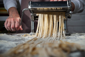 Caucasian female hands making fettuccine noodles using mechanical pasta machine