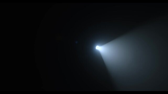 A powerful, focused beam of white light emanating from a spotlight in a dark room is turned toward the camera, creating a lens flare effect. Lighting equipment backstage. Slow motion.