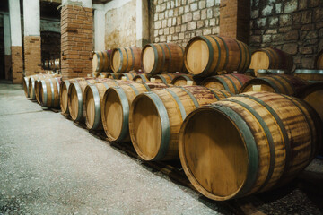 Rows of traditional oak wine barrels aging in a dim, authentic stone cellar of a historic winery