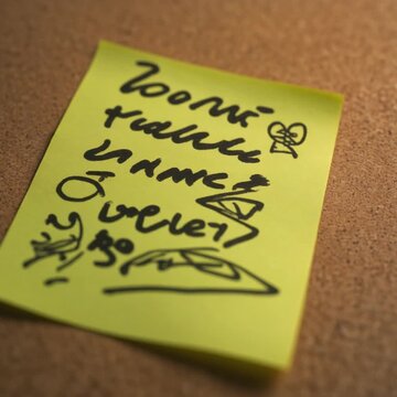 Close-Up of a Handwritten Note with Smiley Face. Retro / Nostalgia / Time Warp. Handwritten note on a brightly colored sticky note featuring messy handwriting doodles and a smiley face icon.
