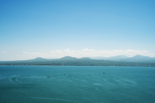 Wide panoramic view of Lake Sevan with turquoise water, small boats, and green mountain shores under a clear blue sky