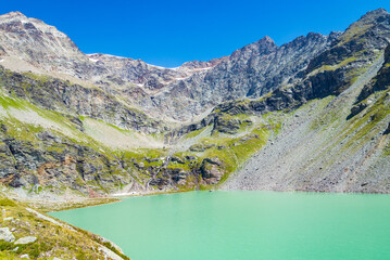 The emerald waters of the "San Grato" lake, Valgrisenche, Aosta Valley, Italy. High rock peaks on the bacgrkound with blue sky.