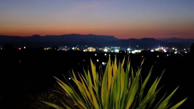 Beautiful sunset sky over small city in mountain valley at dusk, twilight cityscape silhouette with orange and purple horizon background.