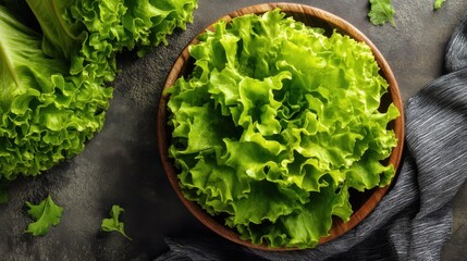 Fresh green leaf lettuce in wooden bowl on dark background.