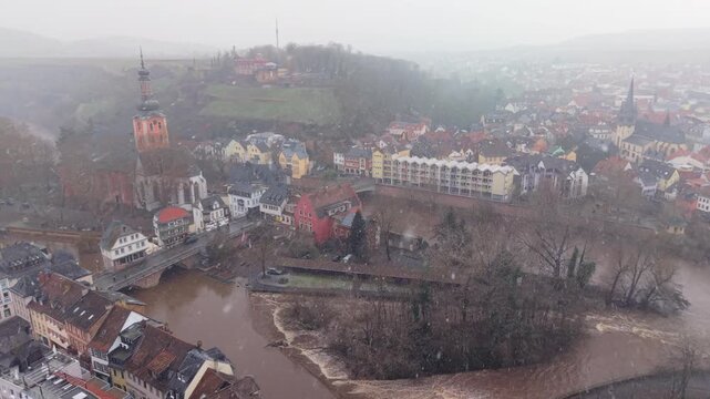Aerial 4K view of historic Br&uuml;ckenh&auml;user bridge houses in Bad Kreuznach during snowfall. Cinematic drone footage of a flooded Nahe river and snow-covered timbered houses in winter