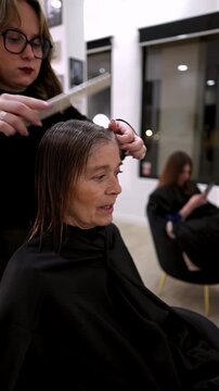 Professional female hairstylist creating beautiful curls and waves on a client's long, healthy brunette hair with a hot iron styler during a hair treatment session in a modern beauty salon