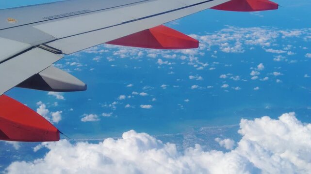 wing plane air thick clouds below land towns sides ocean meeting horizon blue light softens coastal closeup view airplane perspective civilization structure altitude reflection 