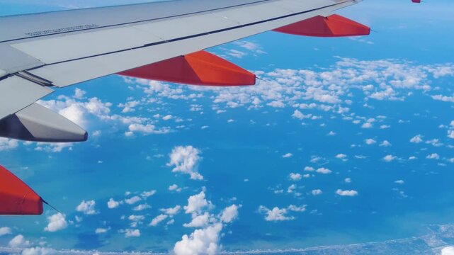 frames wing plane air thick clouds below land towns sides ocean meeting horizon blue light to closeup top down view airplane perspective altitude civilization structure atmosphere 