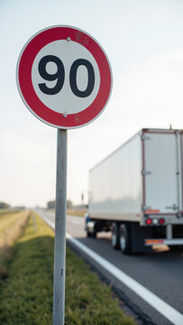 Speed limit sign indicating 90 kilometers per hour on highway with truck in background. scene captures clear day with open road and green grass