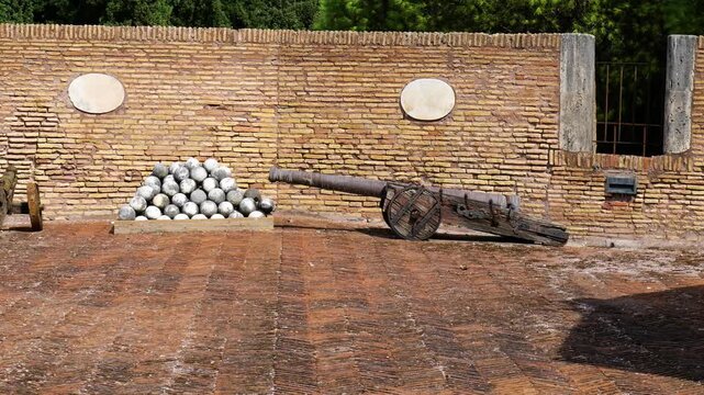 aged cannons wooden carriages flank stacked pyramid stone cannonballs artillery display sits against weathered brick fortification wall historic castel sant'angelo rome italy heavy 