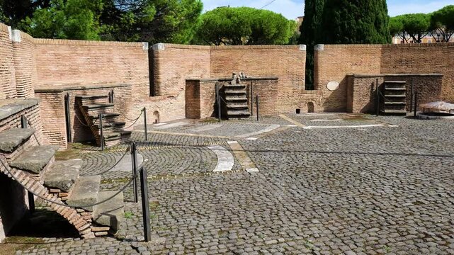 quiet interior courtyard curved cobblestone paving low brick walls niches stone stairways lead elevated platforms framed by tall trees castel sant'angelo to rome italy hadrian's mausoleum 