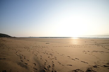 Sunset over a sandy beach with footprints leading toward the water