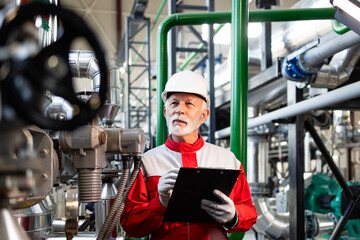 Senior engineer inspecting industrial plant operations with clipboard