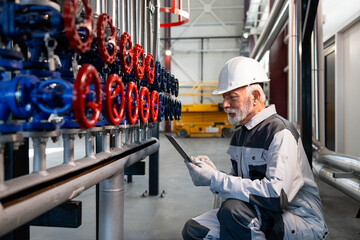 Senior engineer inspecting industrial valves with tablet