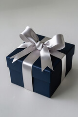 Elegant navy blue gift box adorned with a luxurious silver ribbon bow, perfectly placed on a subtle textured background 