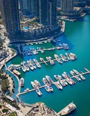 Fototapeta premium Aerial drone view of Dubai Marina harbor with many luxury yachts, capturing modern waterfront and city skyline. Floating boats on canal