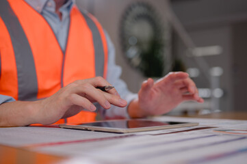 Engineer wearing safety vest using pen and digital tablet working in construction site office discussion project