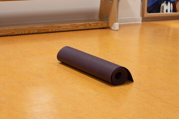 Rolled yoga mat placed on a smooth wooden floor in a bright studio, surrounded by natural light, inviting a peaceful atmosphere for exercise and mindfulness practice