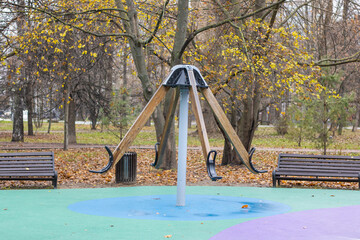Colorful playground amid falling leaves, Peaceful urban park displaying lively playground amidst fallen yellow leaves and overcast sky