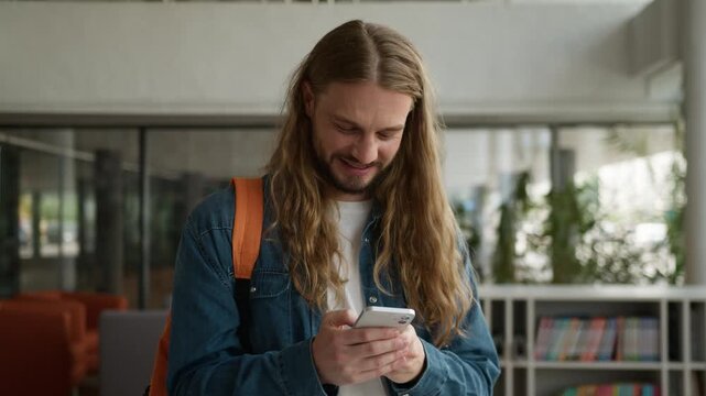 Caucasian man laughing humorous joyful fun holding mobile phone smartphone technology guy male student with cellphone device laugh watching funny content network social media in university college