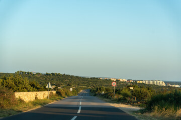 Fototapeta premium Empty country road with 60 km speed limit sign leading to coastal town through green Mediterranean hills on summer evening. Concept of road trip travel, scenic route, driving journey, vacation drive.