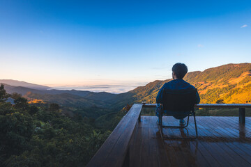 Traveler asian man relax on balcony in homestay resort Doi Sakad mountain valley with fog at sunrise sky in Pua Nan Thailand Winter travel holiday vacation concept