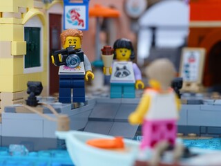 Obraz premium Tambov, Russian Federation - January 05, 2026 Lego man minifigure with camera and a girl with ice cream standing on a dock and looking to a woman in boat.