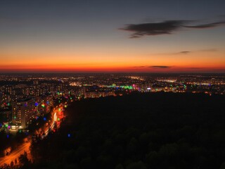 Fototapeta premium Elevated panoramic view of a city at sunset showing bright twilight colors, scattered urban lights, dark forest, and prominent colorful digital glitch artifacts.