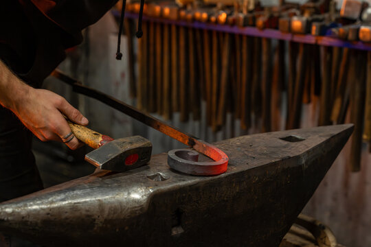 Gros plan sur un forgeron martelant une pi&egrave;ce de m&eacute;tal chauff&eacute;e sur une enclume, illustrant le travail artisanal de forge et la fabrication traditionnelle en ferronnerie.