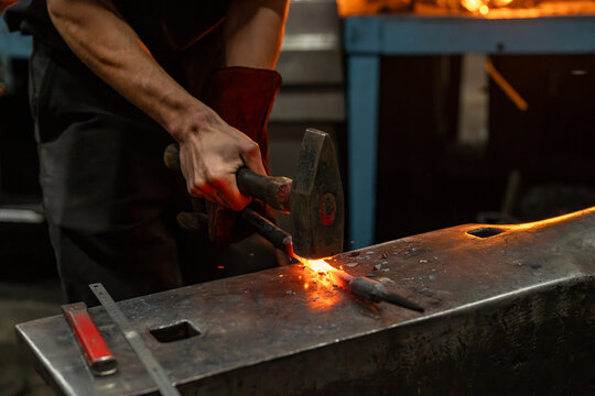 Gros plan sur un forgeron martelant une pi&egrave;ce de m&eacute;tal chauff&eacute;e sur une enclume, illustrant le travail artisanal de forge et la fabrication traditionnelle en ferronnerie.