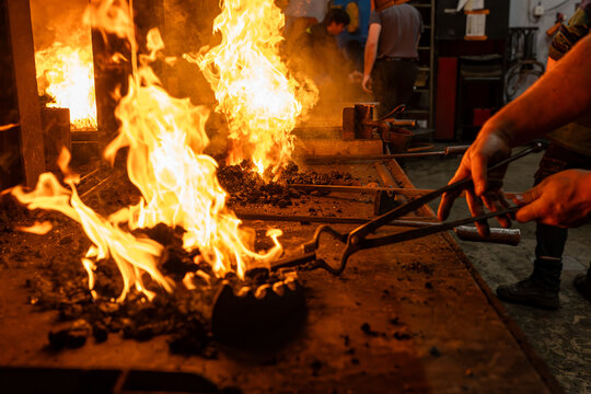 Sc&egrave;ne de forge en atelier avec un artisan manipulant du m&eacute;tal au feu &agrave; l&rsquo;aide de pinces, illustrant la puissance du travail traditionnel de ferronnerie.