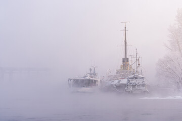 The outlines and silhouettes of old river ships moored to the shore in the winter fog. nostalgic...