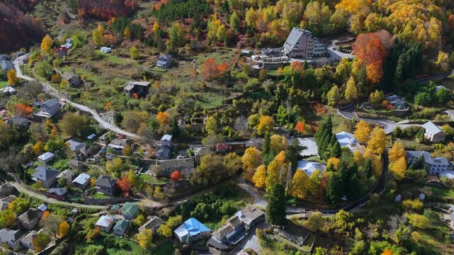 Autumn aerial video of Dardh&euml; with hillside homes, vibrant trees and layered mountain slopes lit by warm seasonal sunlight.