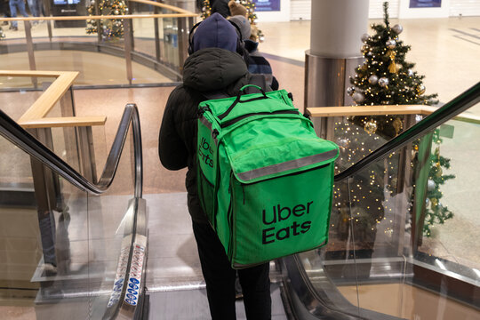 Krakow, Poland - November 30, 2025: Uber Eats delivery person with green bag on escalator, reflecting urban convenience during festive season in a mall