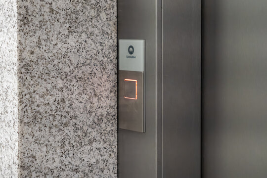 Krakow, Poland - November 30, 2025: Schindler elevator call button illuminated with a bright orange light, signaling readiness for use in a sleek, modern building environment