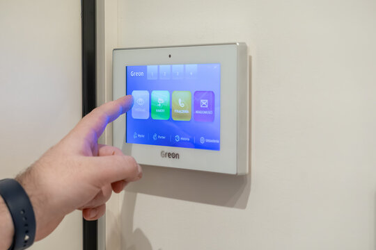 Krakow, Poland - November 30, 2025: Person's finger engages a smart home video intercom system display, managing modern dwelling security and reliable visitor access control