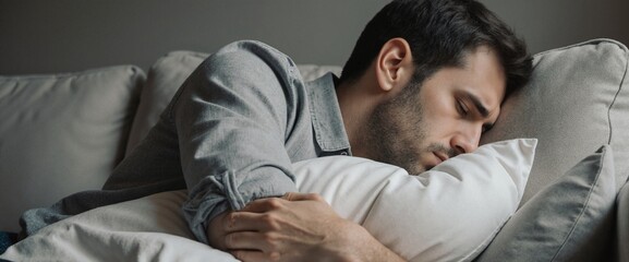Man seated on a couch embracing a pillow thinking about problems. Deep in thought, emotions like stress, sadness, or exhaustion. Loneliness concept