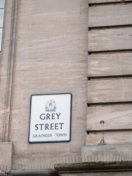 Grey Street sign mounted on a pale stone wall in Grainger Town, Newcastle, featuring classic architecture and urban detail.
