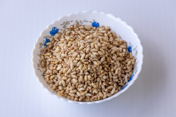 Close-up of crunchy puffed brown rice served in a white ceramic bowl against a white backdrop. Popularly called muri, murmura, and khoi, used for healthy breakfast or light snack food.