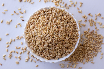 A white ceramic bowl filled with puffed brown rice. Known as muri, murmura, and khoi, these light grains are a popular ingredient in traditional Indian and Bengali snacks. Top view.