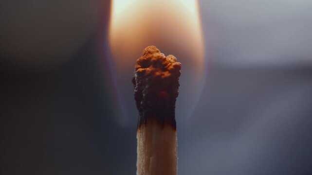 Extreme close-up view of match head being lit with bright flame, then burning and forming glowing halo around charred tip