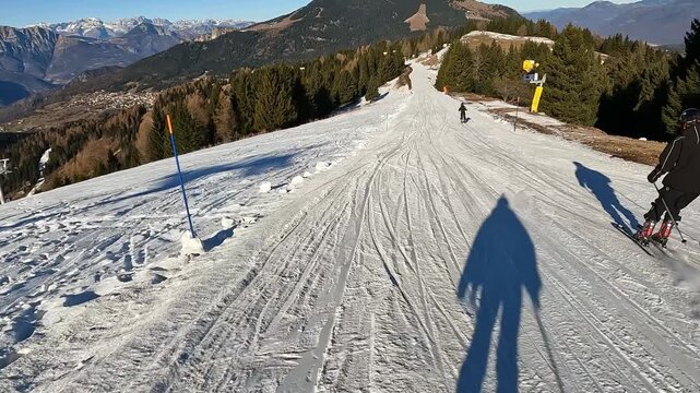 Following a skier carving on wide groomed slope in Folgaria ski resort, Italian Alps winter sports action. Skier carving on white slope during sunny winter day in Folgaria, Italian Alps ski resort wit