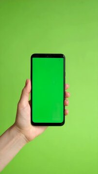 Person holding a smartphone with green screen display against a bright green backdrop for app mockups and visual content insertion