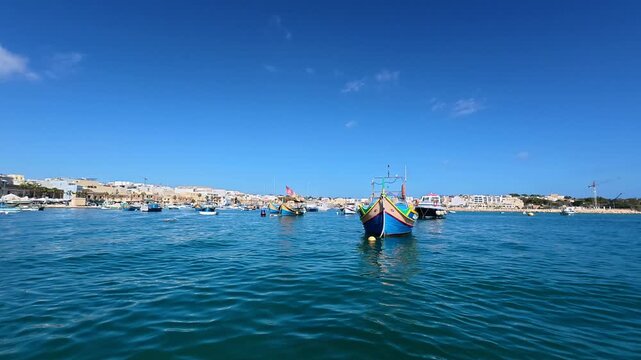 Cinematic 4K slow motion footage of colorful traditional Luzzu fishing boats floating in Marsaxlokk harbor, Malta. View from a moving boat capturing the scenic Mediterranean fishing village, historic 